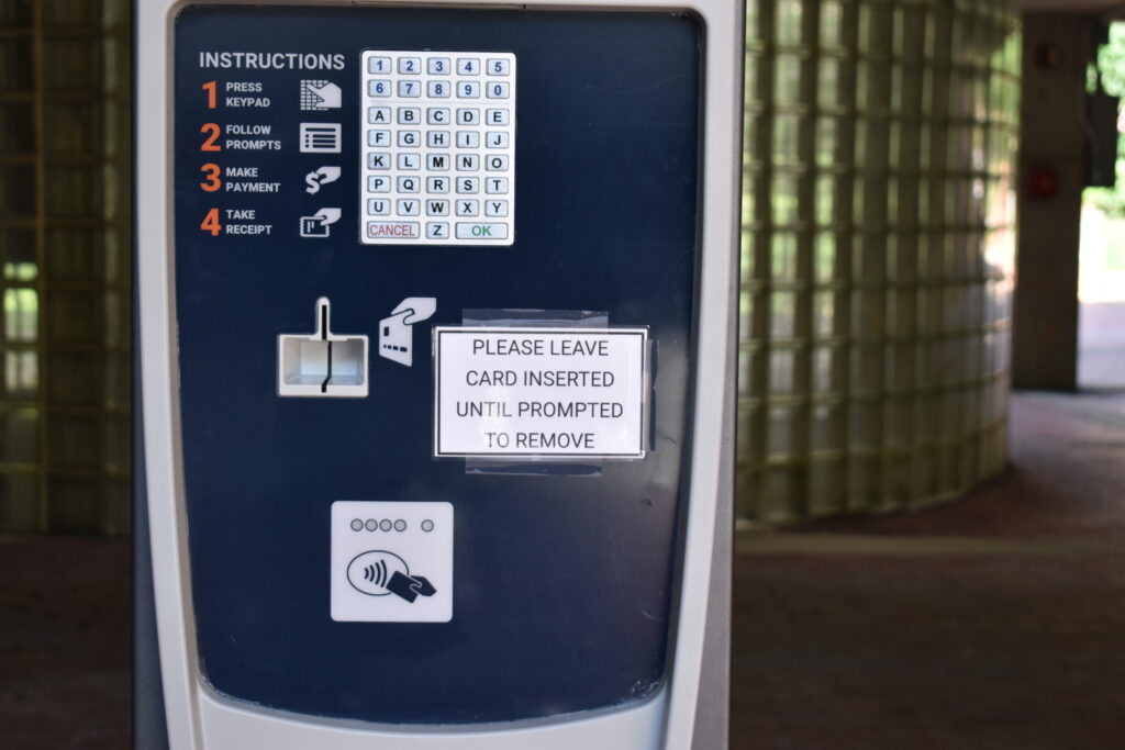 Picture of paystation with sign reminding users to leave their card in until prompted to remove it.