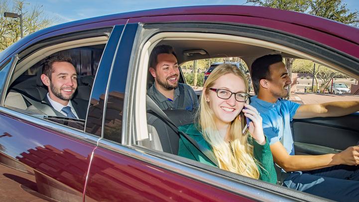 Four people inside a maroon sedan, with the front passenger talking on her phone.