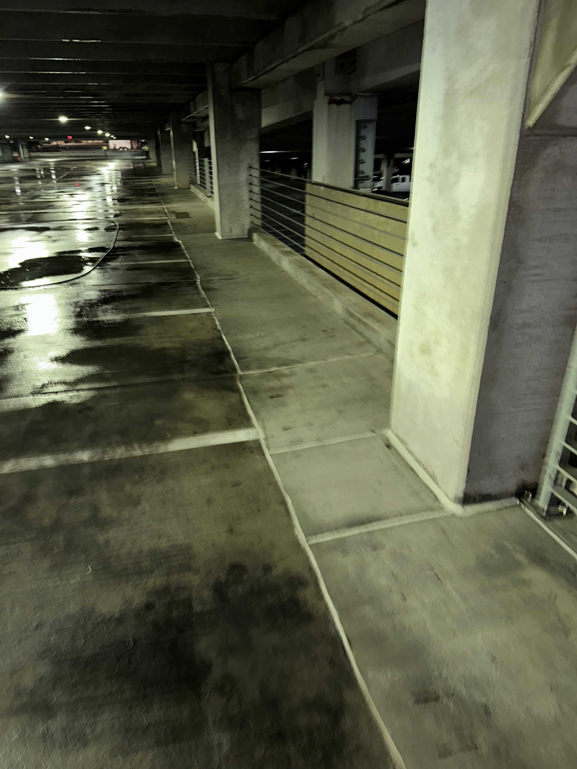 Dimly lit parking garage with wet concrete floors and reflective patches.