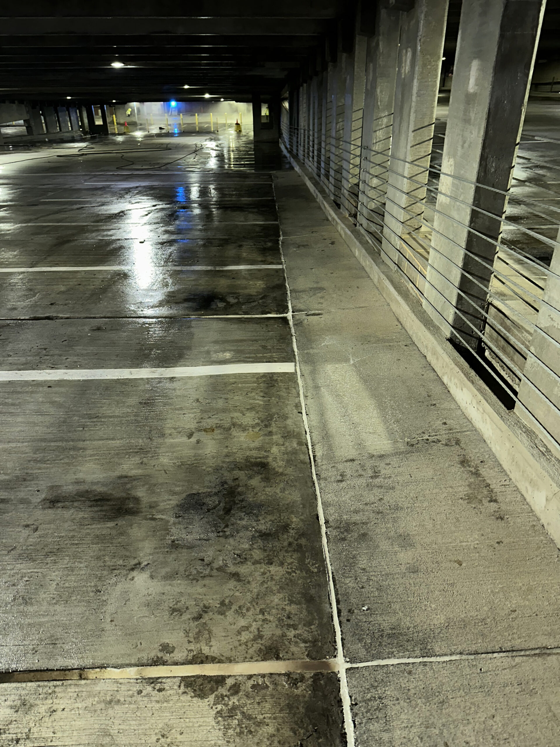 Empty wet parking garage with concrete pillars and bluish lights in the background.