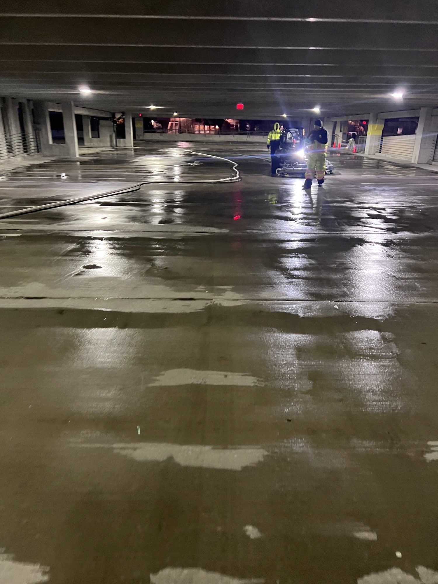 Wet indoor parking garage with two people in safety gear near equipment.