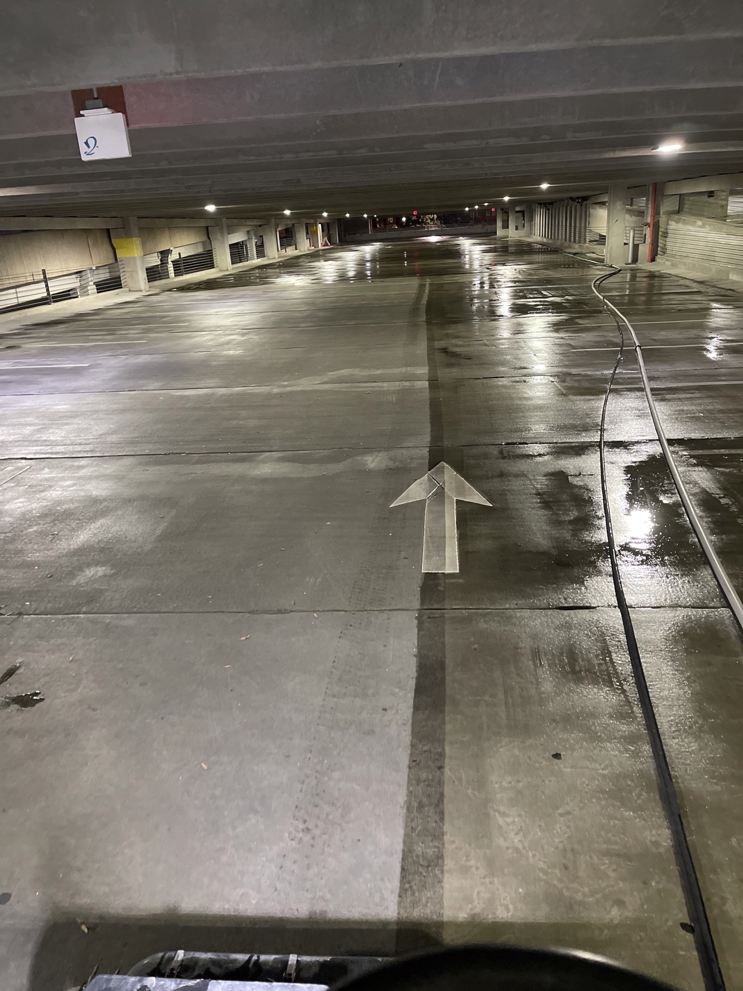 Empty indoor parking garage with wet concrete floor and overhead lighting.