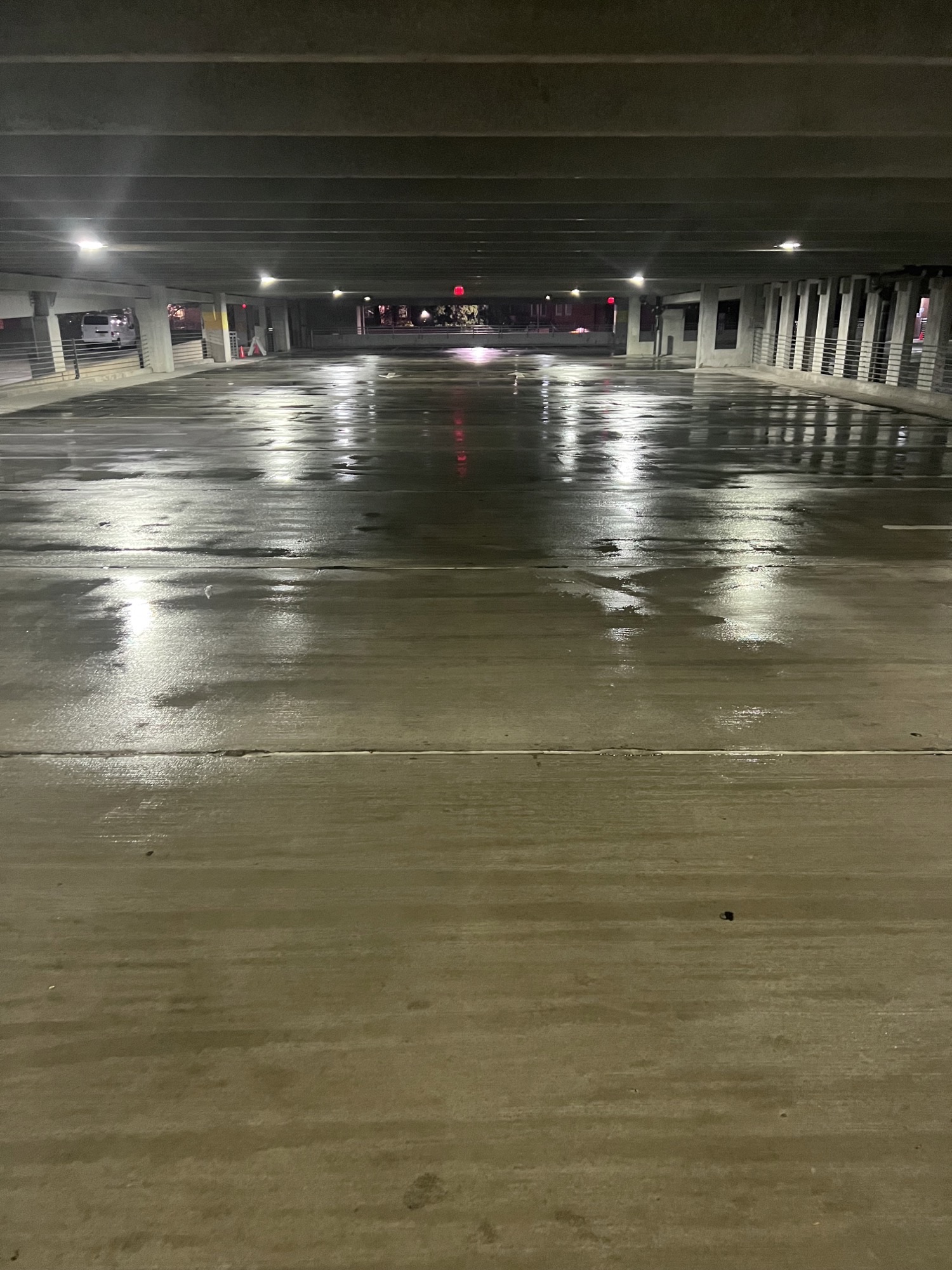 Empty parking garage with wet floor reflecting ceiling lights at night.