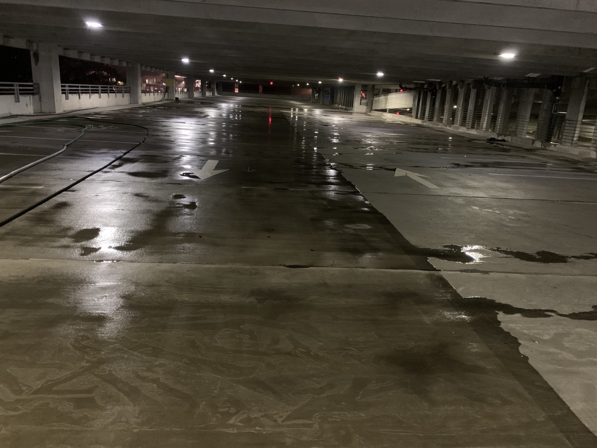 Dimly lit parking garage with a wet, reflective floor and overhead lights.