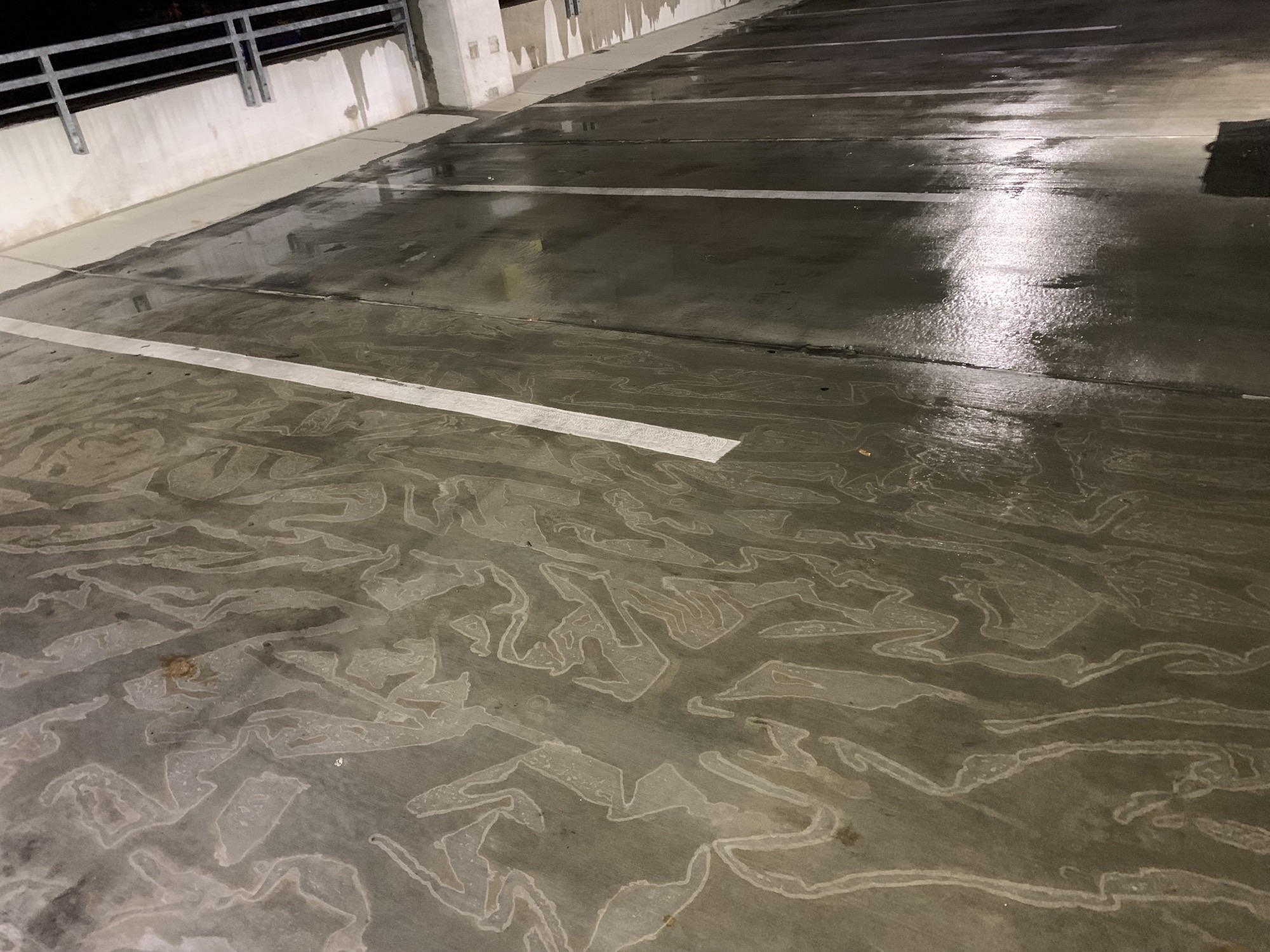 A wet concrete parking lot with reflective surfaces and swirling patterns under artificial light.