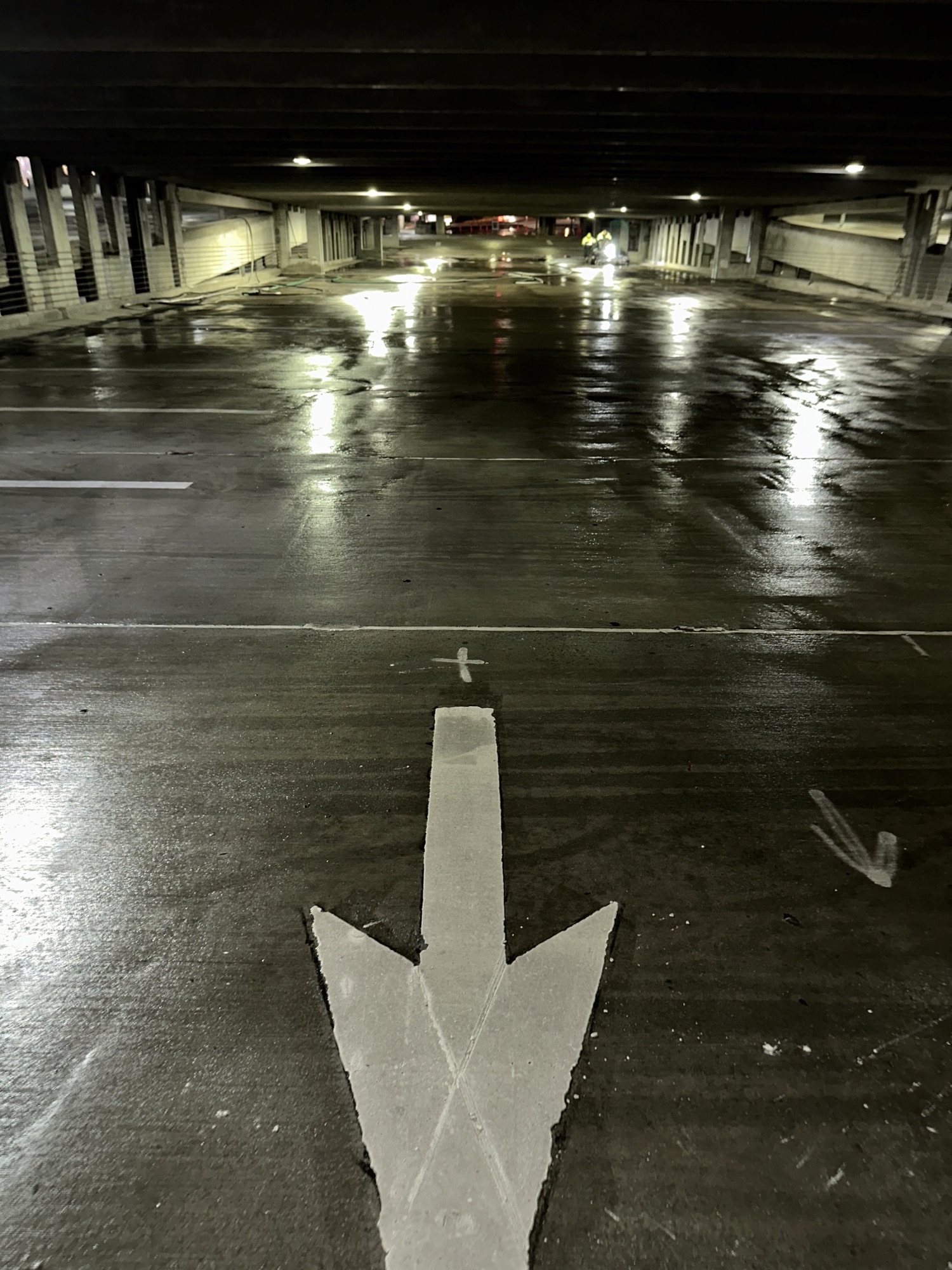 An empty parking garage with wet floors and a large white arrow pointing forward.