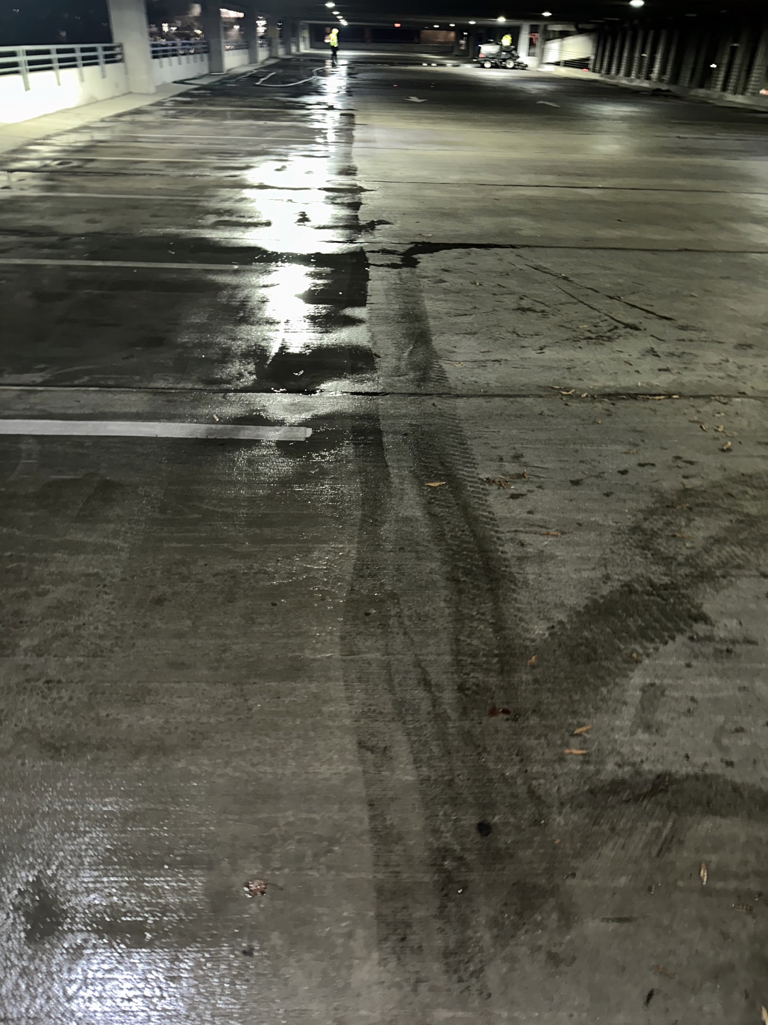 Empty wet parking garage with reflected lights and tire marks on the floor.