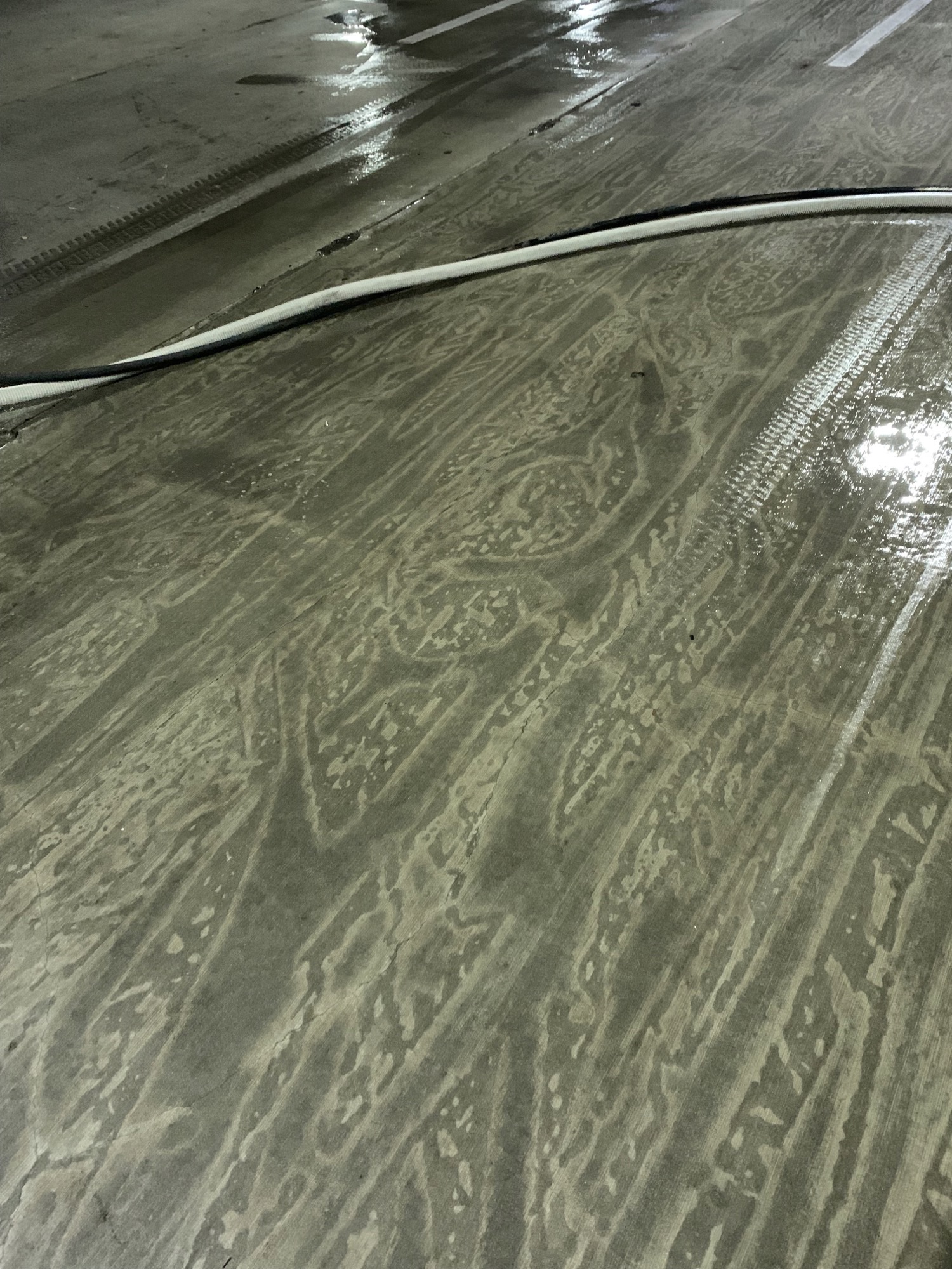 Close-up of a wet concrete surface with intricate patterns, crossed by a black and white hose.
