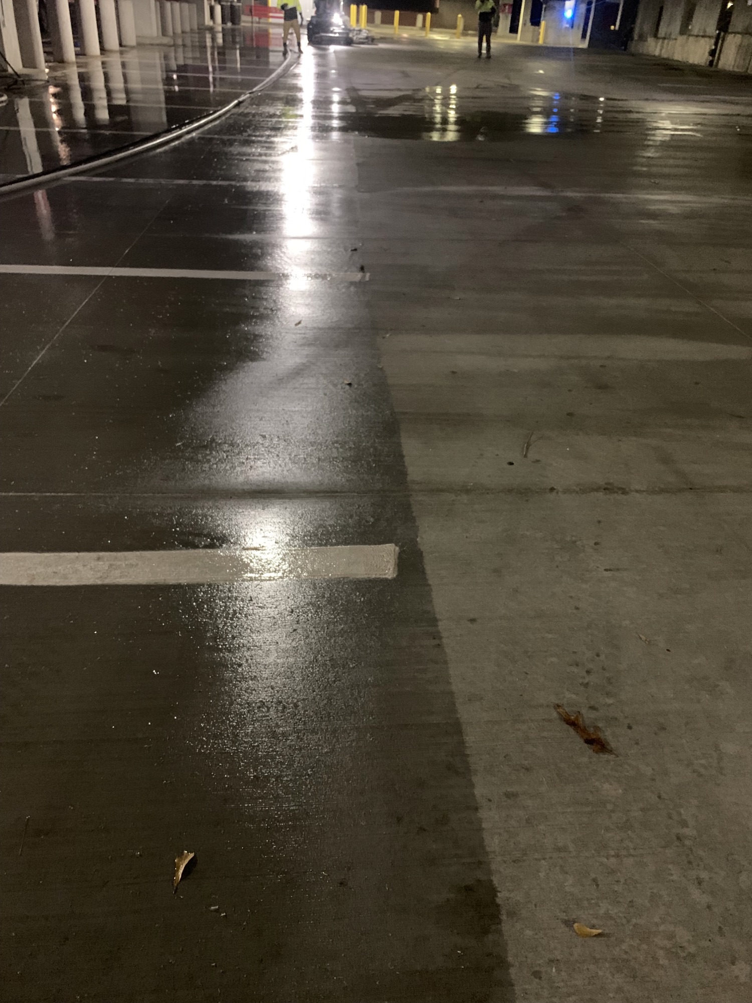 Wet parking garage floor at night with reflections and two figures in the distance.