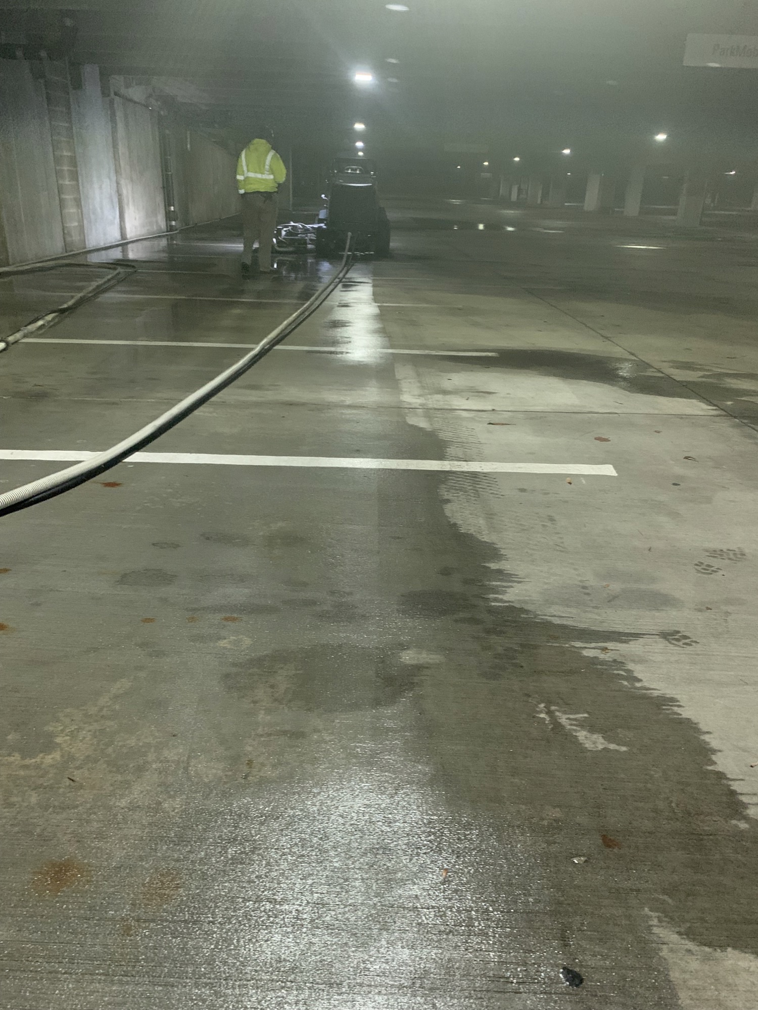 A person cleaning the floor of a wet, dimly lit parking garage.