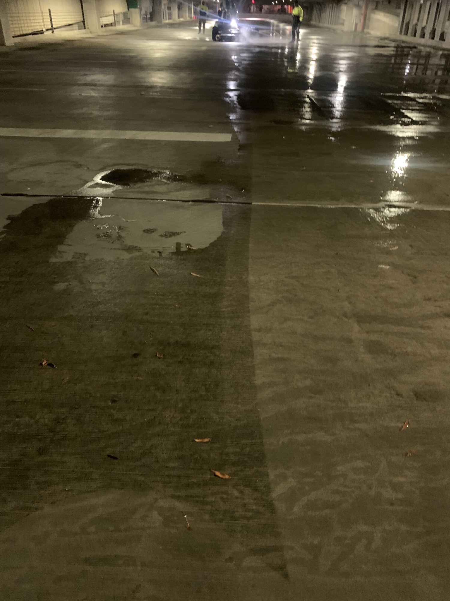 Dimly lit parking garage with wet floors and workers operating a cleaning machine.