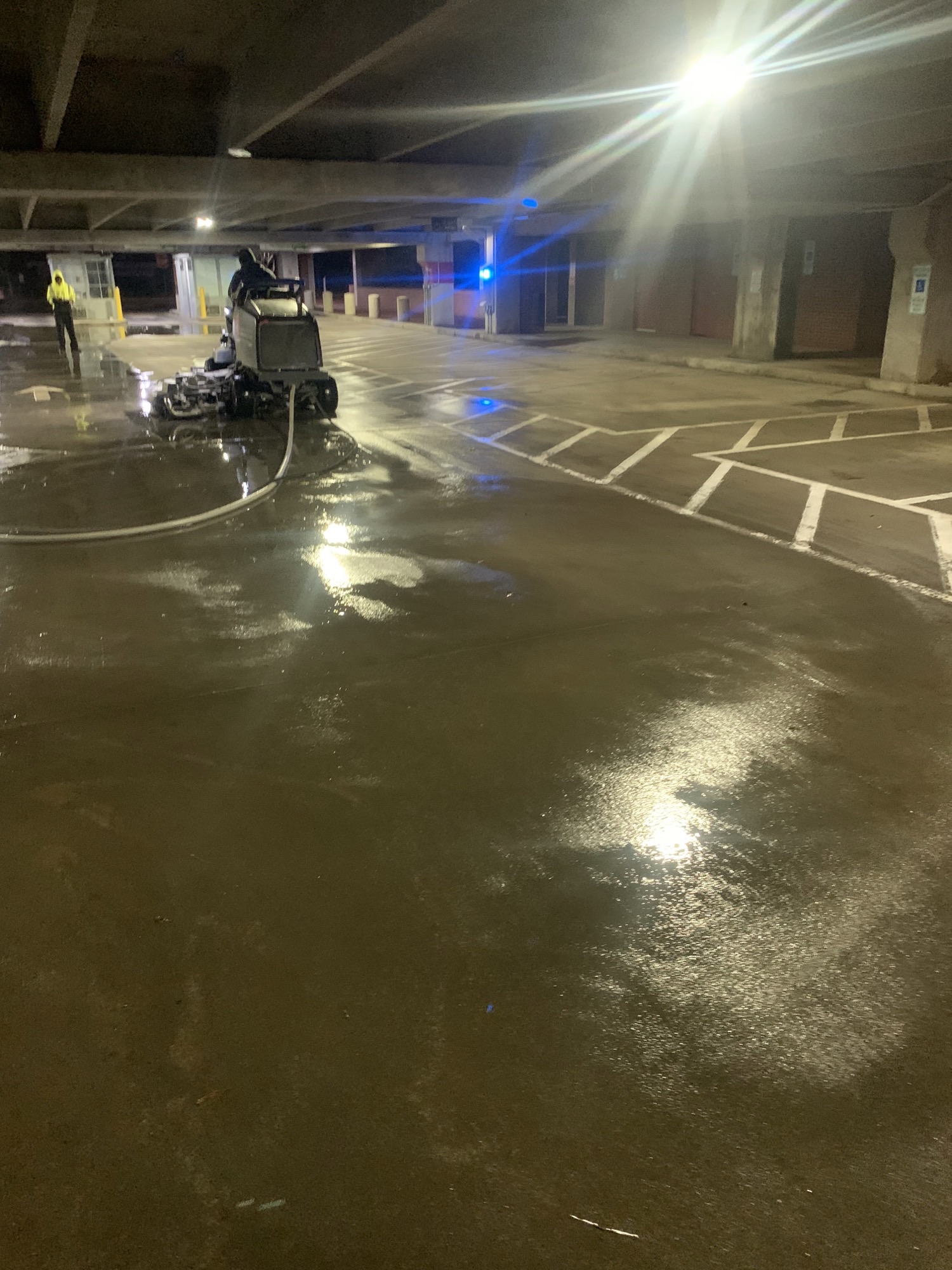 Worker operating a ride-on cleaning machine in a wet parking garage.