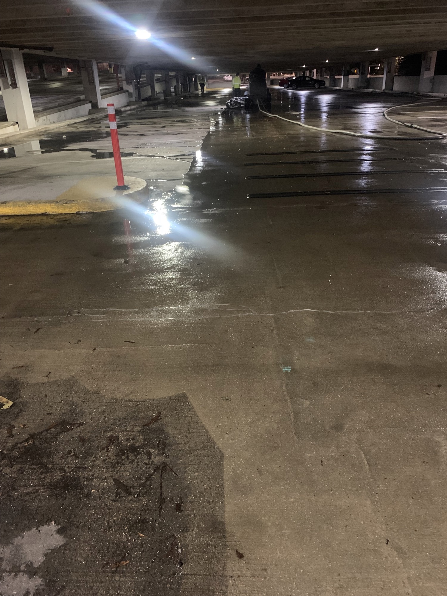 A dimly lit parking garage with a wet concrete floor and overhead lights reflecting on the surface.