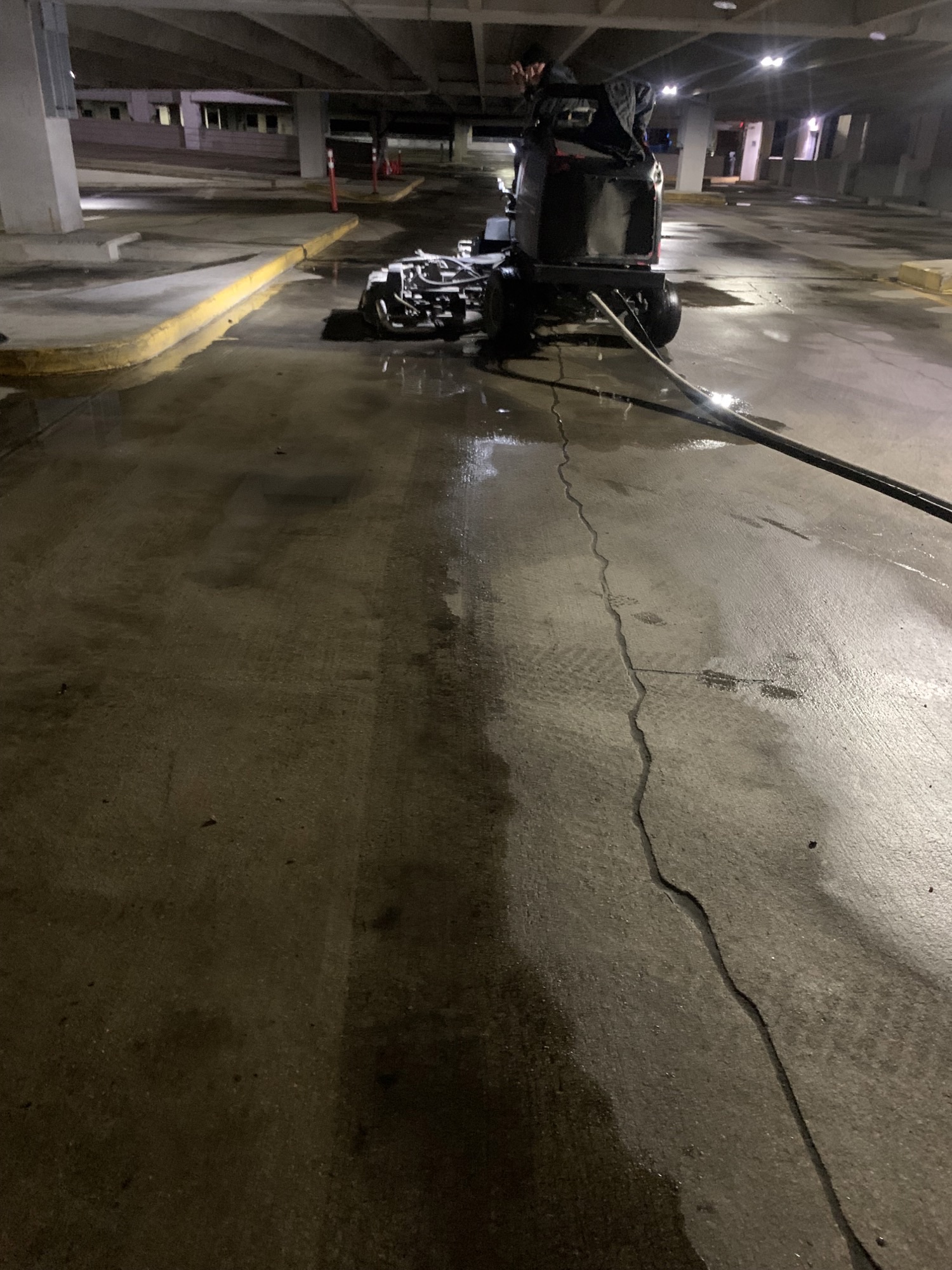 A cleaning machine operating in a dimly lit parking garage with wet concrete floors.