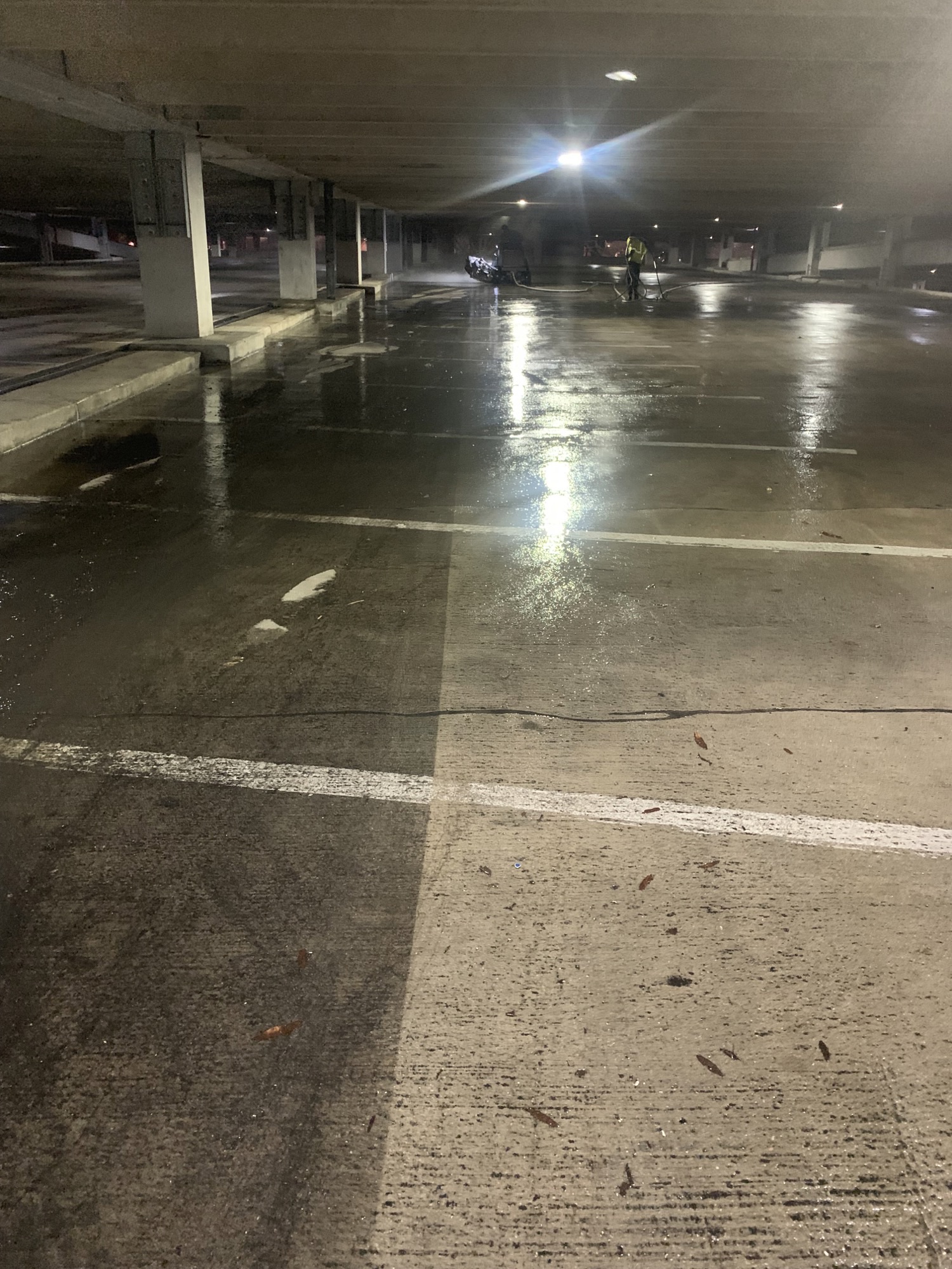 Dimly lit parking garage with wet concrete floors and two figures in the distance cleaning.